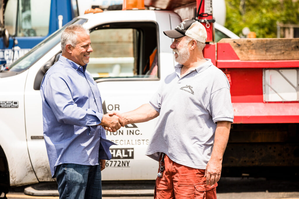 A picture of a man shaking hands with another man in front of a service truck