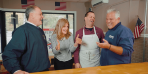 Picture of people in a kitchen with someone with an apron on