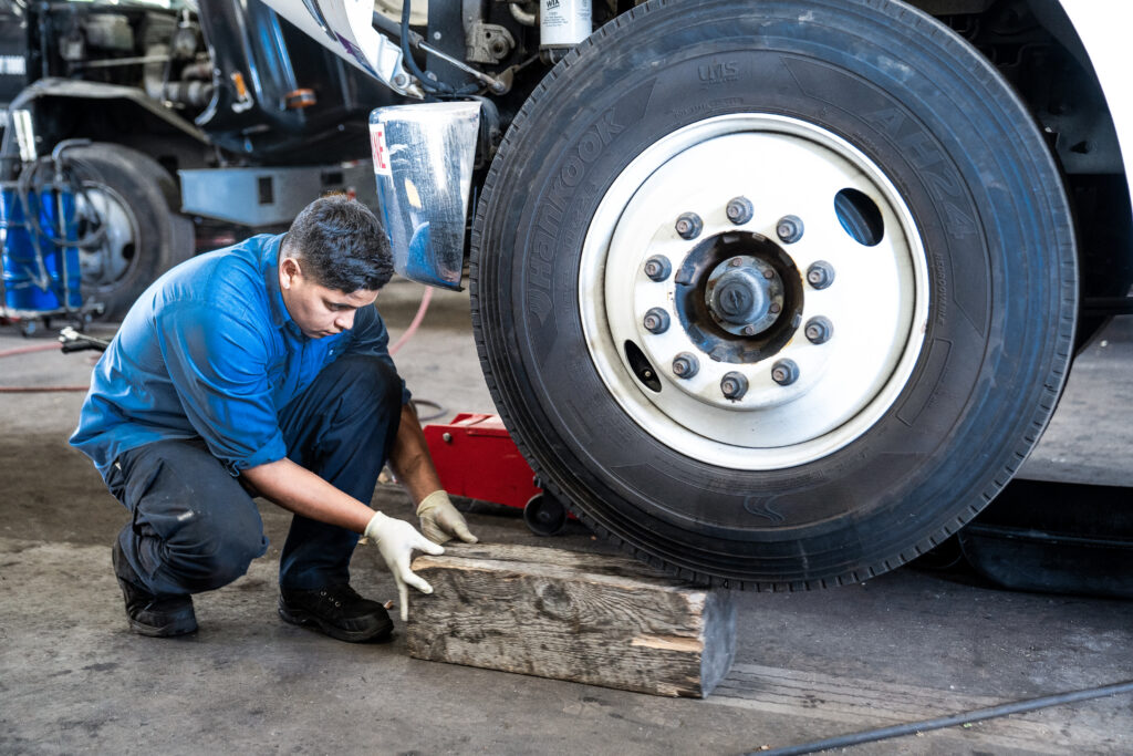 A picture of a person kneeling to place a chock underneath a truck tire