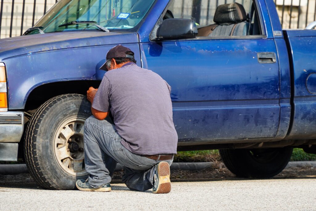 A person working on their pickup truck and kneeling over the tire to fix the tire pressure